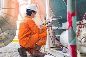Electrician operator inspect and checking heating ventilated and air conditioning (HVAC), air conditioning, electrical service in offshore oil rig platform while worker charging refrigerant in system.